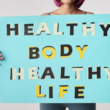 A woman holds a motivational poster advocating a healthy body and life for wellness.